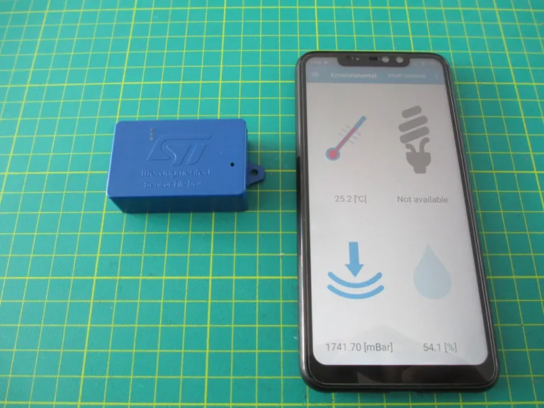Modrá vývojová deska SensorTile.box vedle telefonu s aplikací pro zobrazení údajů ze senzorů