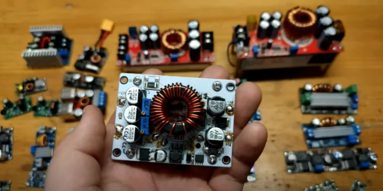 Různé elektronické měniče s cívkami a součástkami, jeden držený v ruce