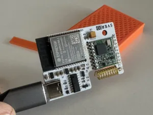 Deska expLORA s konektorem USB a pružinovou anténou na oranžovém podstavci