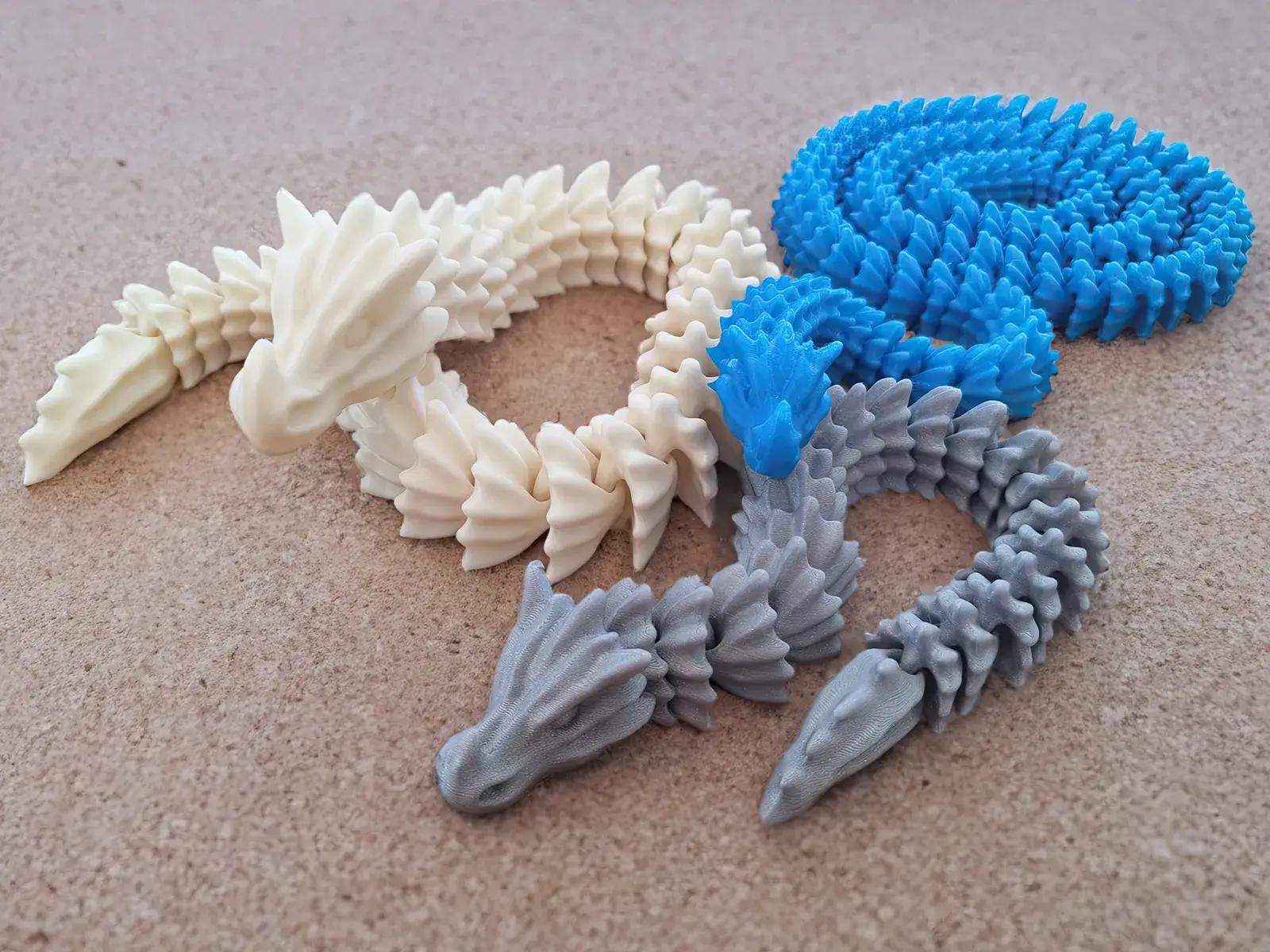 Tři barevné 3D tištěné ohebné figurky draků na stole