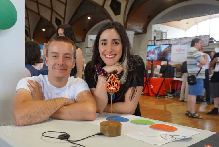 Dva lidé s vystaveným 3D tištěným modelem a fotografiemi bastlířských projektů