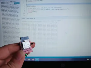 Ruka drží modul ESP32-C3F před obrazovkou s prostředím Arduino IDE
