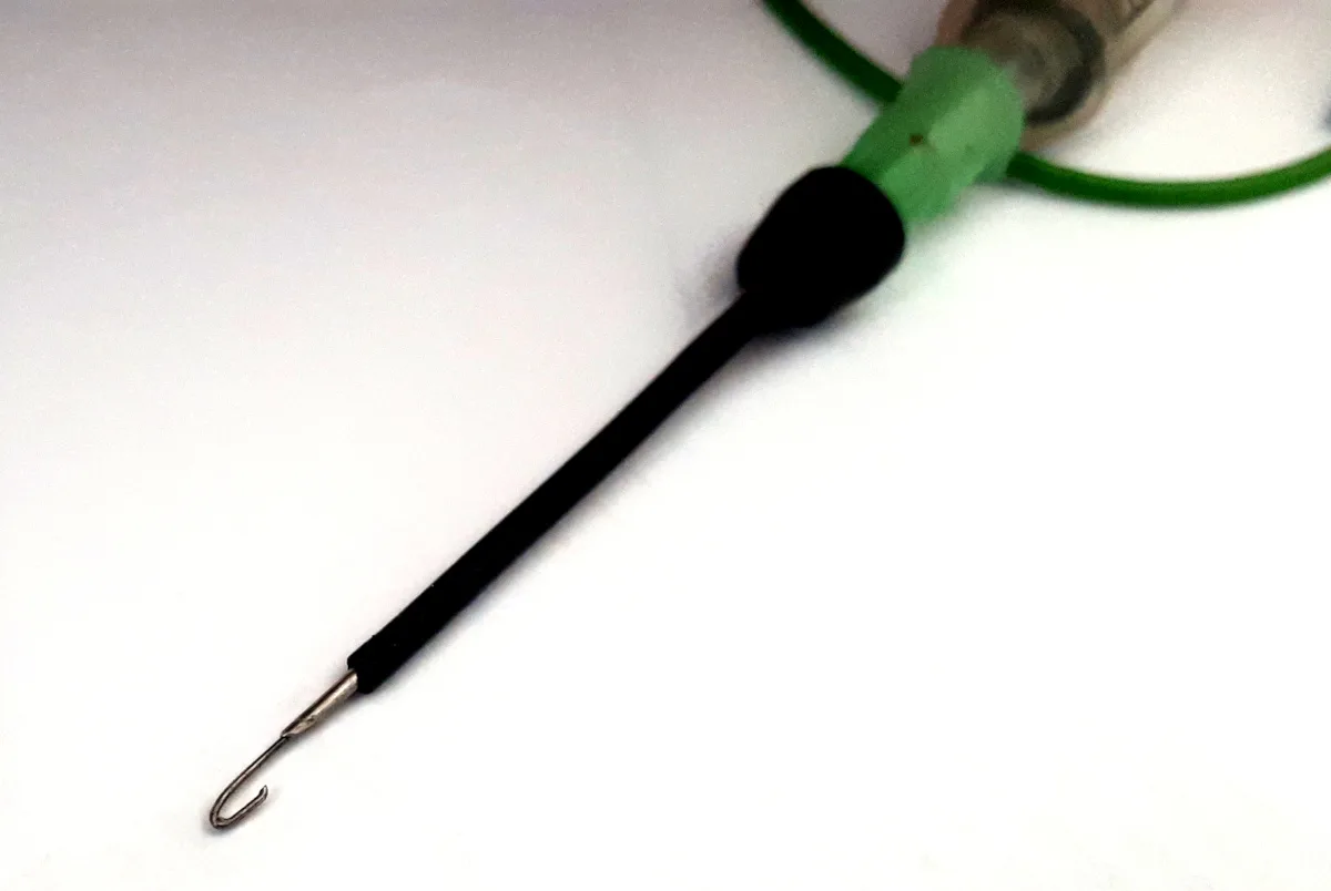Zelený měřicí kabel zakončený černým háčkem s kovovou špičkou