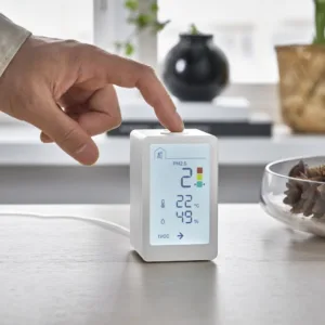 Monitor kvality vzduchu IKEA VINDSTYRKA s displejem, kterého se dotýká prst