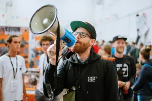 Návštěvník Maker Faire Praha drží u obličeje modrý 3D tištěný přístroj