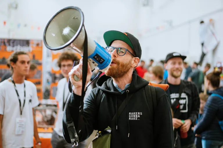 Návštěvník Maker Faire Praha drží u obličeje modrý 3D tištěný přístroj