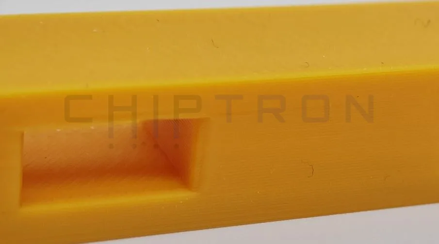 Detail žlutého 3D tištěného hranolu s otvory pro testování přemostění filamentu