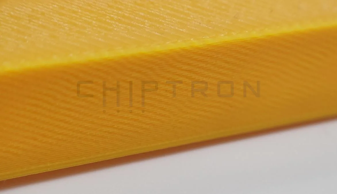 Detail jantarově žlutého 3D tištěného hranolu s otvory pro testování přemostění