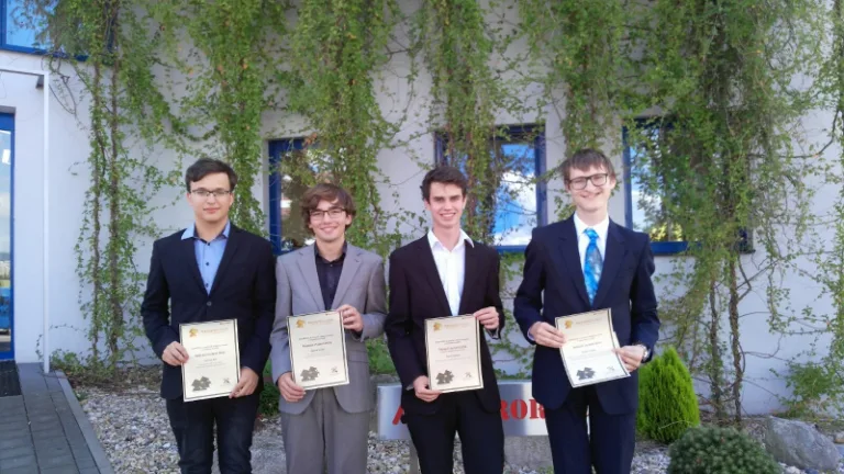 Čtyři studenti drží diplomy před budovou