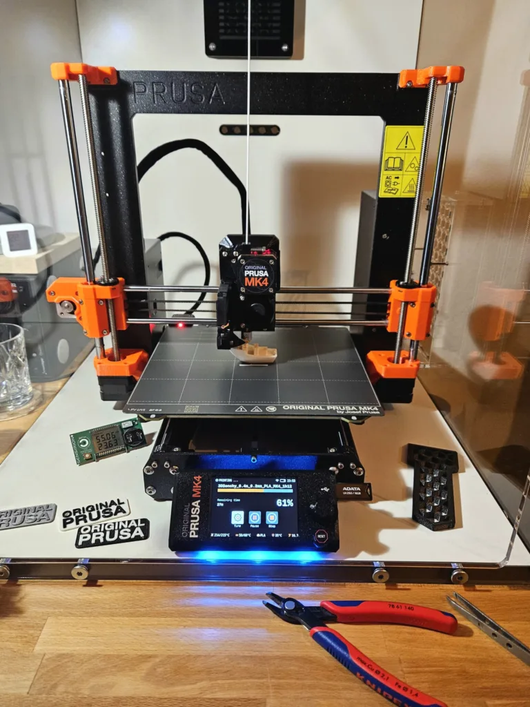 Černooranžová 3D tiskárna Prusa MK4 na stole