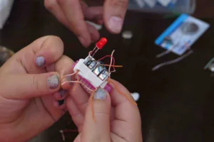 Ruce sestavují malé elektronické zařízení s LED diodou a vodiči