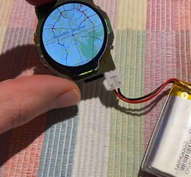 Hodinky Open Smart Watch s kruhovým displejem zobrazujícím mapu, připojené k akumulátoru