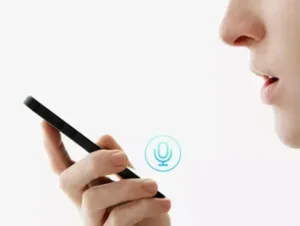 Ruka drží telefon u úst, na obrazovce svítí ikona mikrofonu