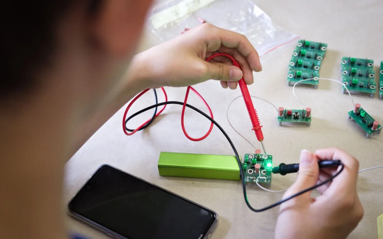 Ruce připojují měřicí sondy k malé elektronické desce na stole