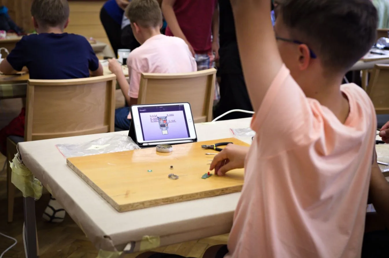 Děti na robotickém táboře programují zařízení u pracovního stolu