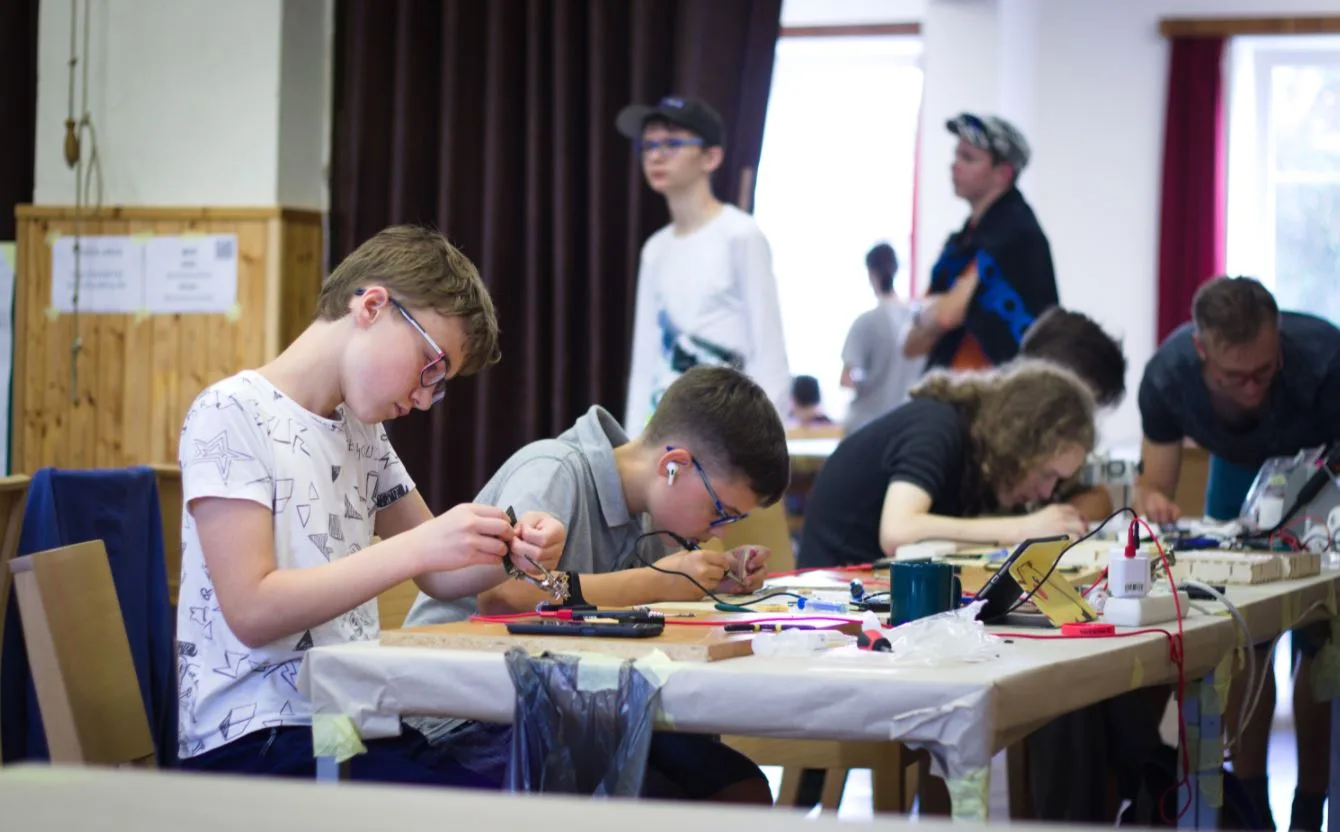 Děti na robotickém táboře sestavují elektronické obvody u pracovního stolu