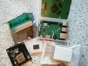 Jednodeskový počítač RockPi 4B vedle eMMC modulu, PoE modulu a krabičky
