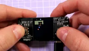 Ruce drží malý TFT modul Adafruit s barevným displejem a popisky pinů
