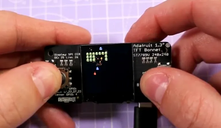 Ruce drží malý TFT modul Adafruit s barevným displejem a popisky pinů