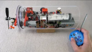 Řez modelem ponorky s elektronikou a vrtulí, vedle něj dálkový ovladač