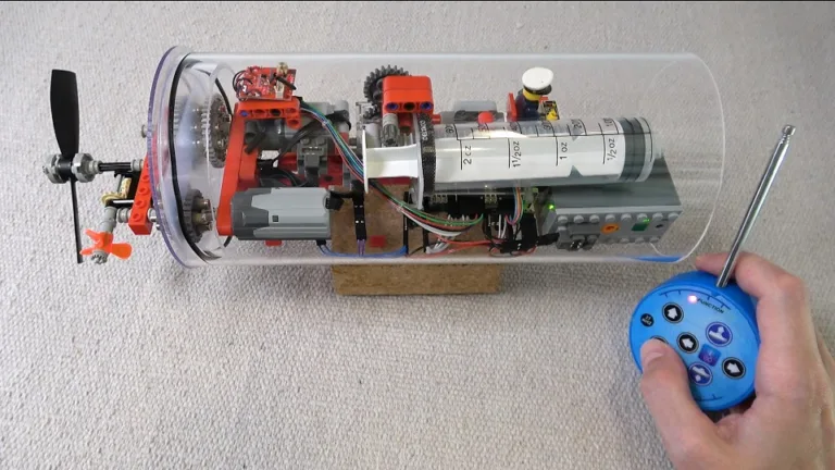 Řez modelem ponorky s elektronikou a vrtulí, vedle něj dálkový ovladač