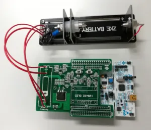AA bateriový tester s otevřenou elektronikou a červenými měřicími vodiči