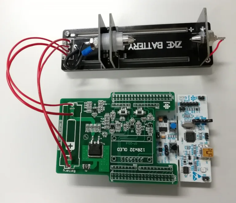 AA bateriový tester s otevřenou elektronikou a červenými měřicími vodiči