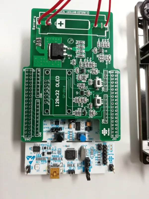 Zelený měřicí adaptér s elektronikou a připojenými vodiči pro testování AA baterií